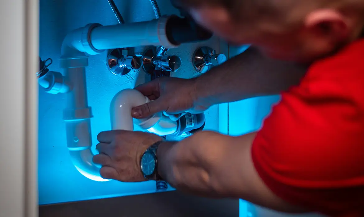 Man fixing pipes under sink